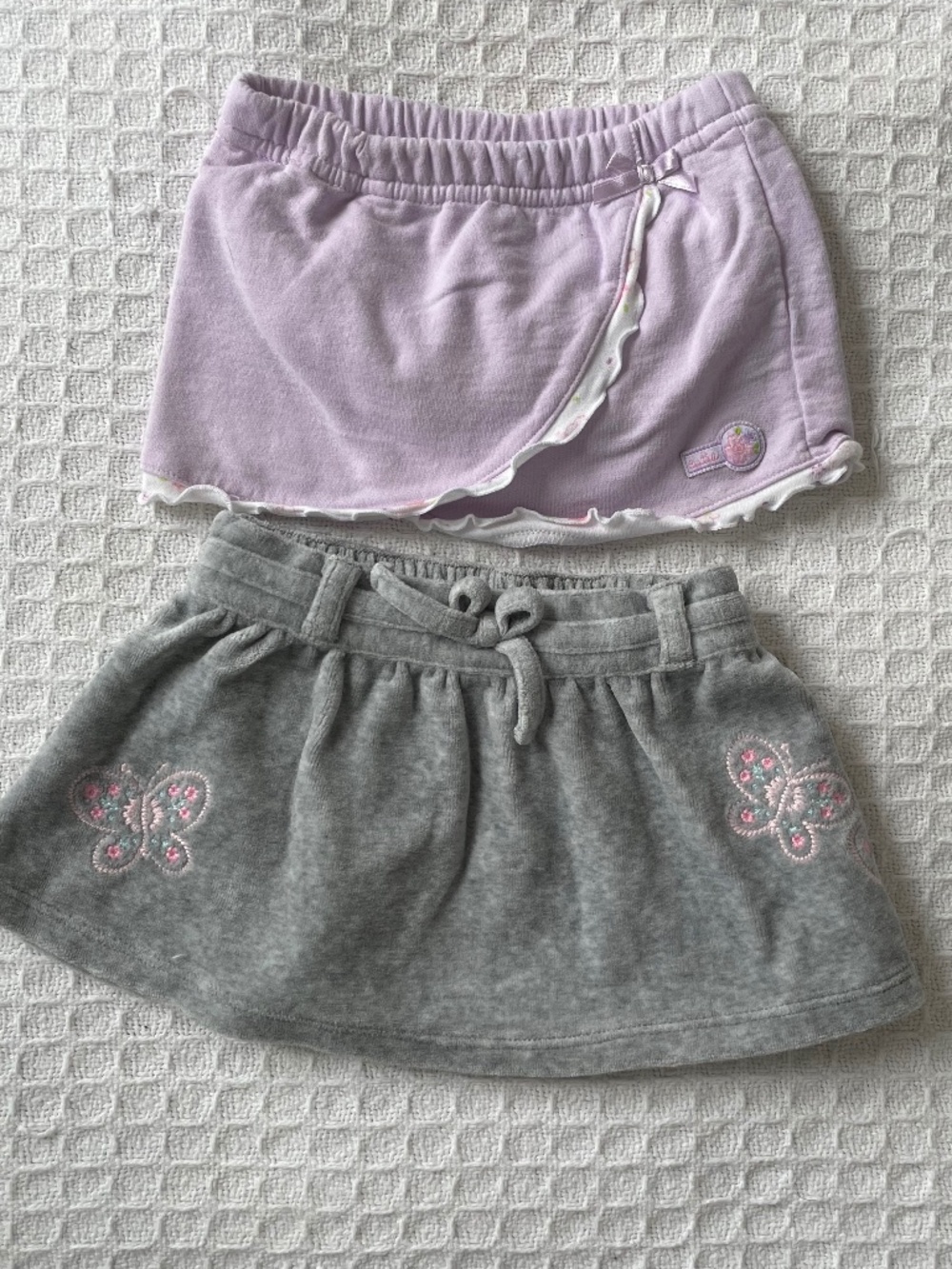 2 girls skirts - 1 lavender and 1 grey w/embroidered butterfly detail, both 3-6m